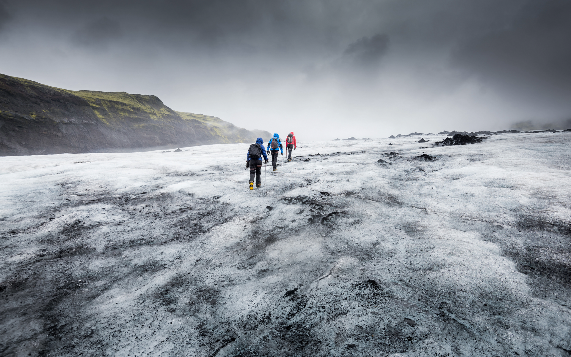 A few or a family or group of friends climbing up a snowy mountain hill with lots of essential hiking and climbing gear and it's white and misty and very cloudy as they work their way up towards the sky.